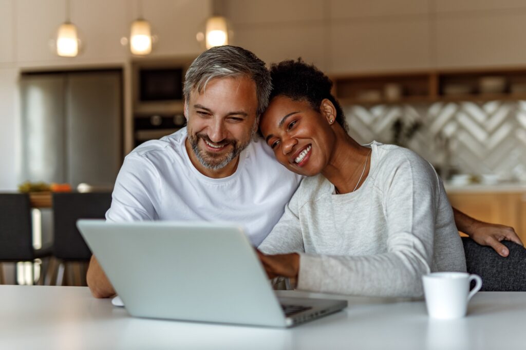 Couple sitting at a table together while looking at a laptop screen