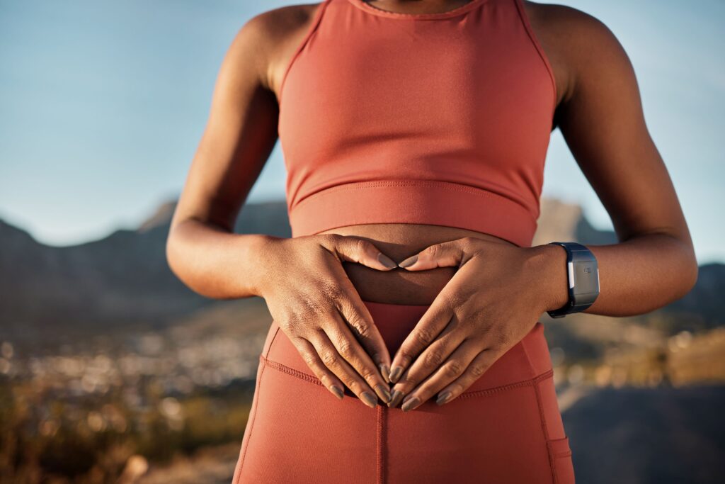 Woman wearing fitness clothing and making a heart with her hands over her stomach out in nature